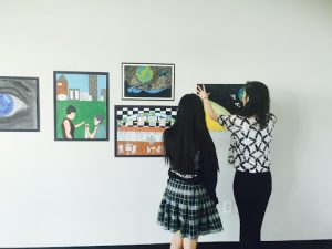 The author and a student hang their art exhibition at a local gallery.