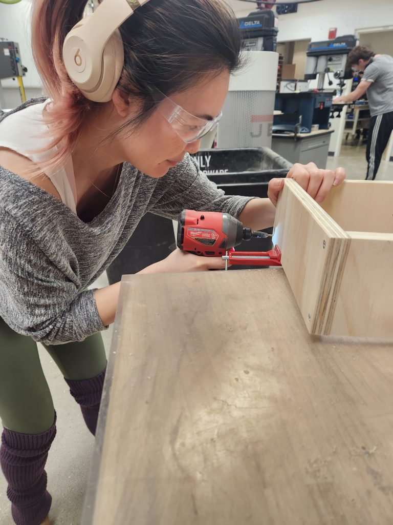 Sharon Tang in headphones screwing in a board with a Makita brand drill