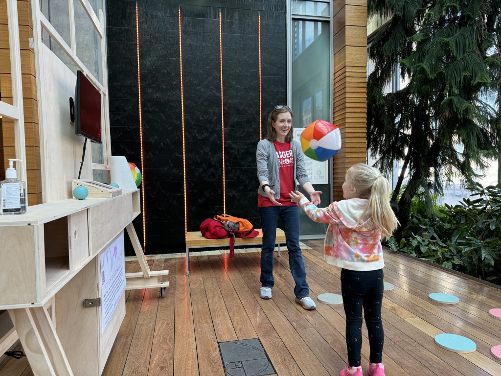 Woman and child play with a beach ball in front of the monitor in the Discovery Building