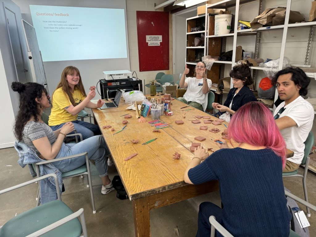 Kohler Fellows around a large wooden table making clay figures
