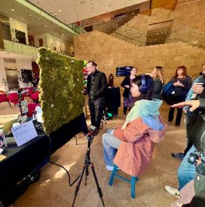 a group of people gather around the moss wall as a person in headphones experiences it.