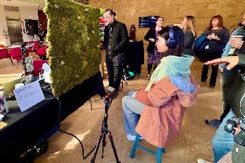 a group of people gather around the moss wall as a person in headphones experiences it.